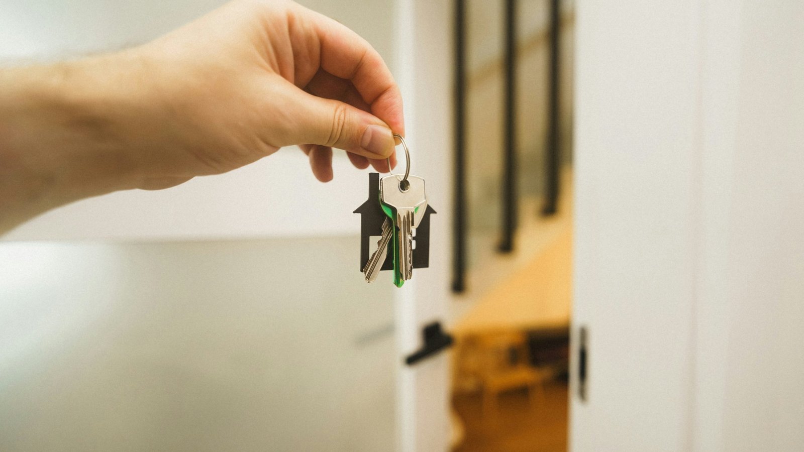 Hand holding a set of house keys on a house-shaped key ring in front of an open interior door