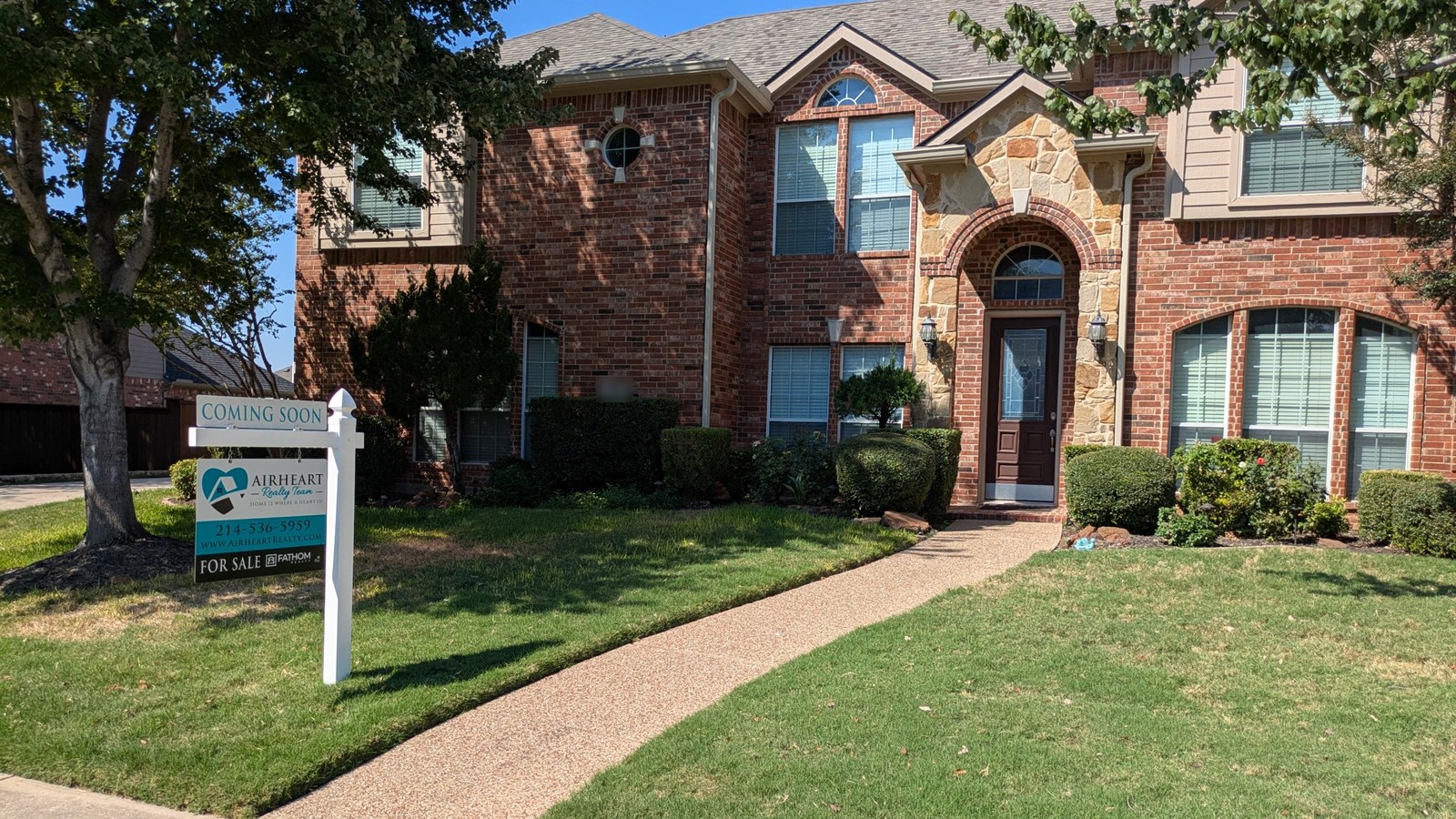 Airheart Realty Team Coming Soon sign in front of a two-story brick home with a stone-arch entry and a green front lawn
