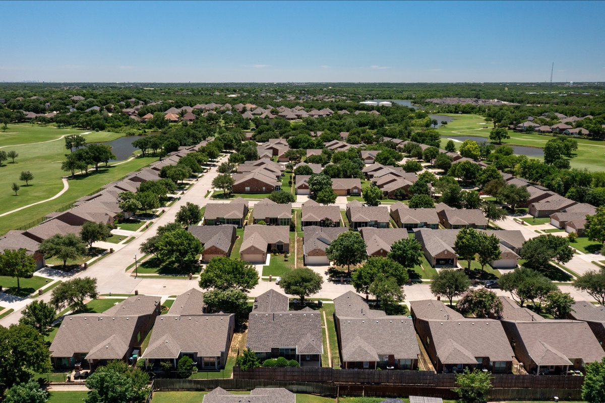 Aerial view of brick single-story homes in the Greens of Oakmont beside the Oakmont Country Club golf course and ponds in Denton, Texas