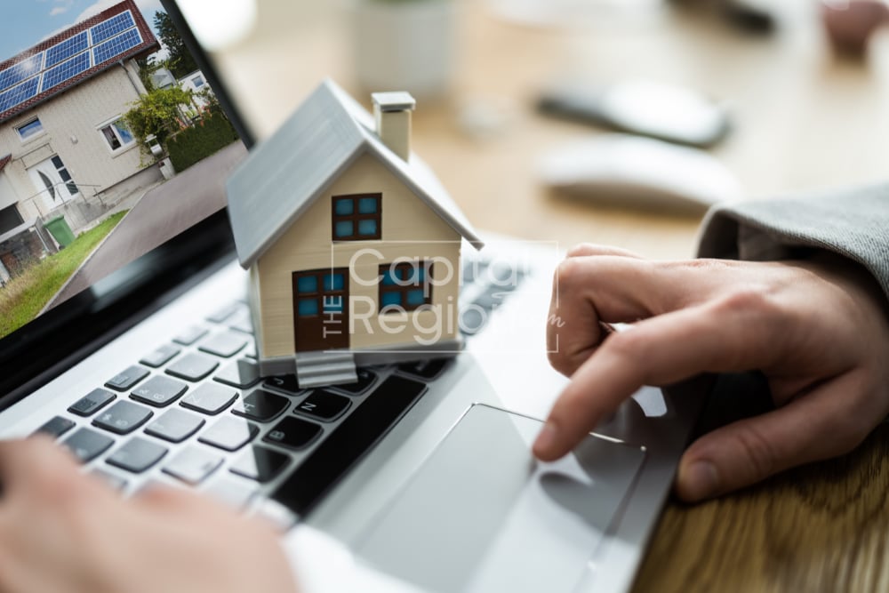 Model house on a laptop showing a solar-panel home, beside a hand using the trackpad.