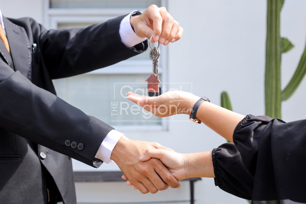 Two people shake hands as one hands over house keys.