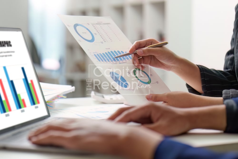 People review printed charts beside a laptop displaying bar graphs.