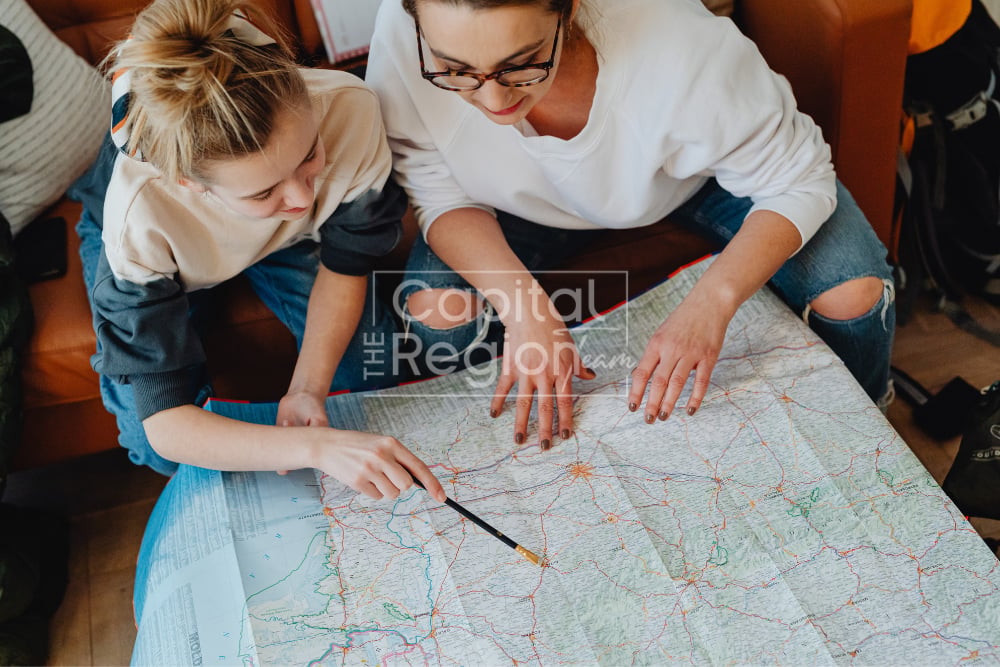 Two women study a large road map together, pointing out routes and locations.