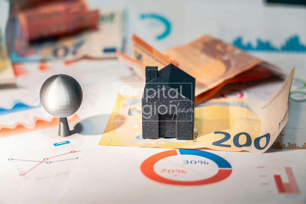Miniature house model on euro banknotes and financial charts.