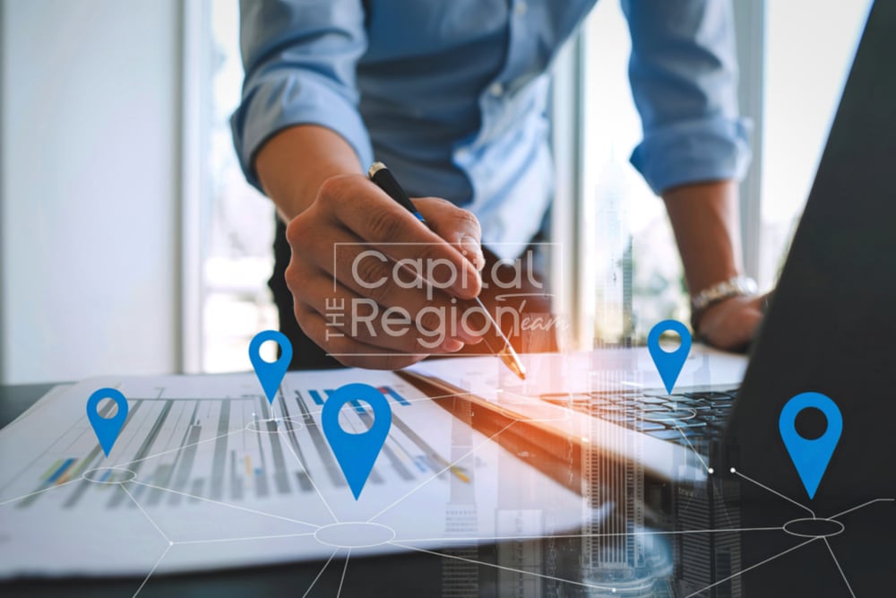 Person reviewing location charts beside a laptop, with blue map pins overlaid.
