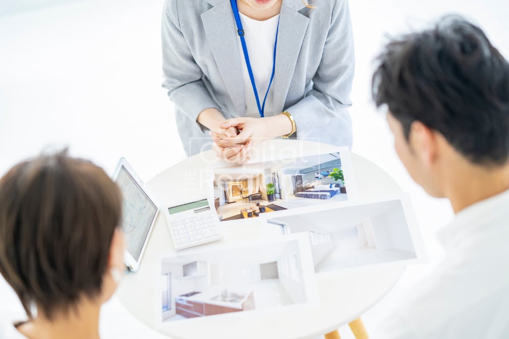 Real estate agent reviews home photos with two clients around a table.