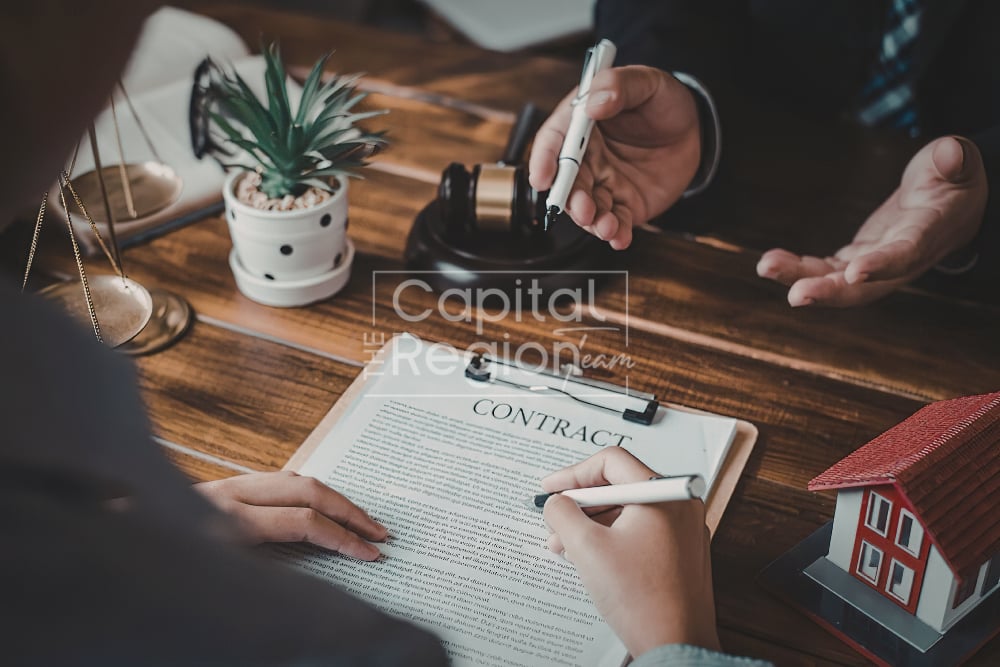 People sign a real estate contract beside a model house on a wooden table.