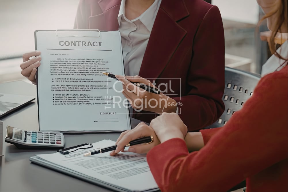Two people review and sign a contract at a desk beside a calculator.