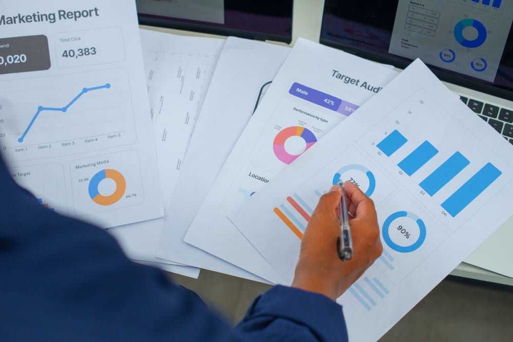 Person reviewing marketing reports and marking a chart with a pen.
