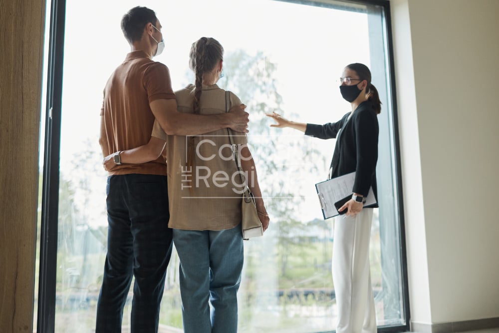 A masked real estate agent shows a couple a home’s large window.