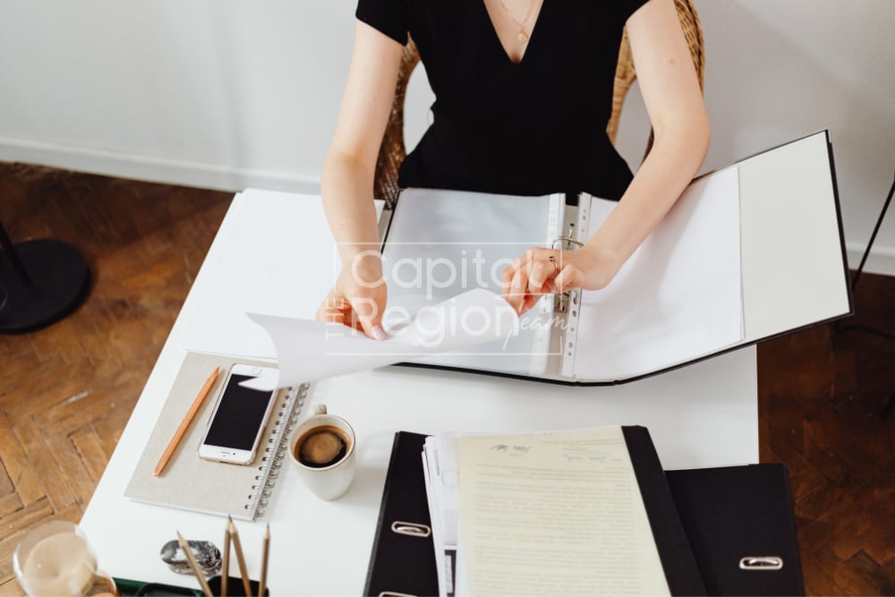Woman sorting papers in a binder at a desk with coffee, a phone, and real estate documents.