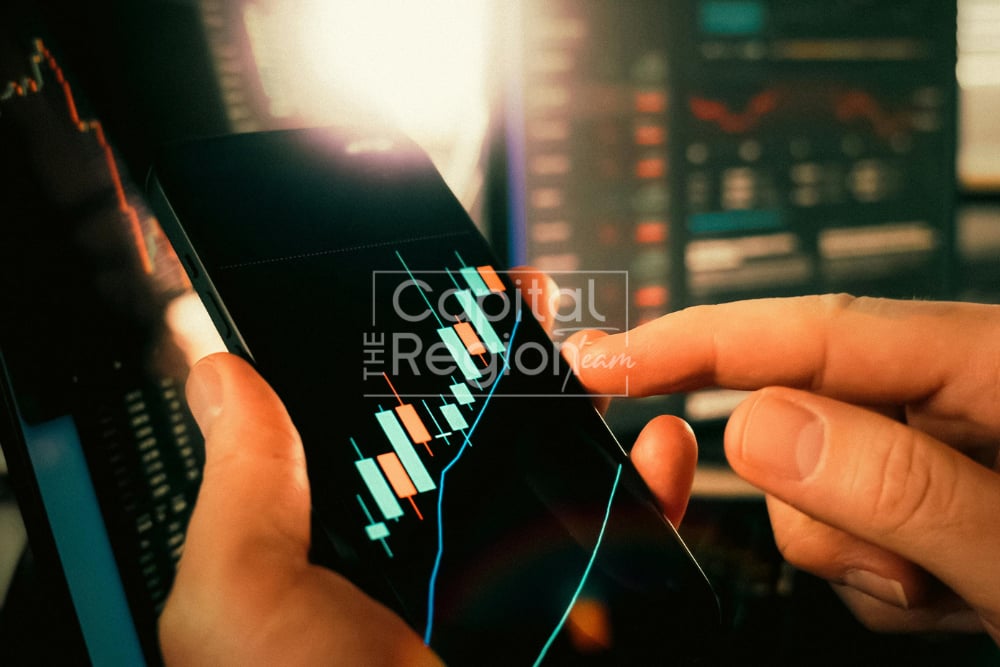Hands use a smartphone displaying a rising chart against blurred financial screens.