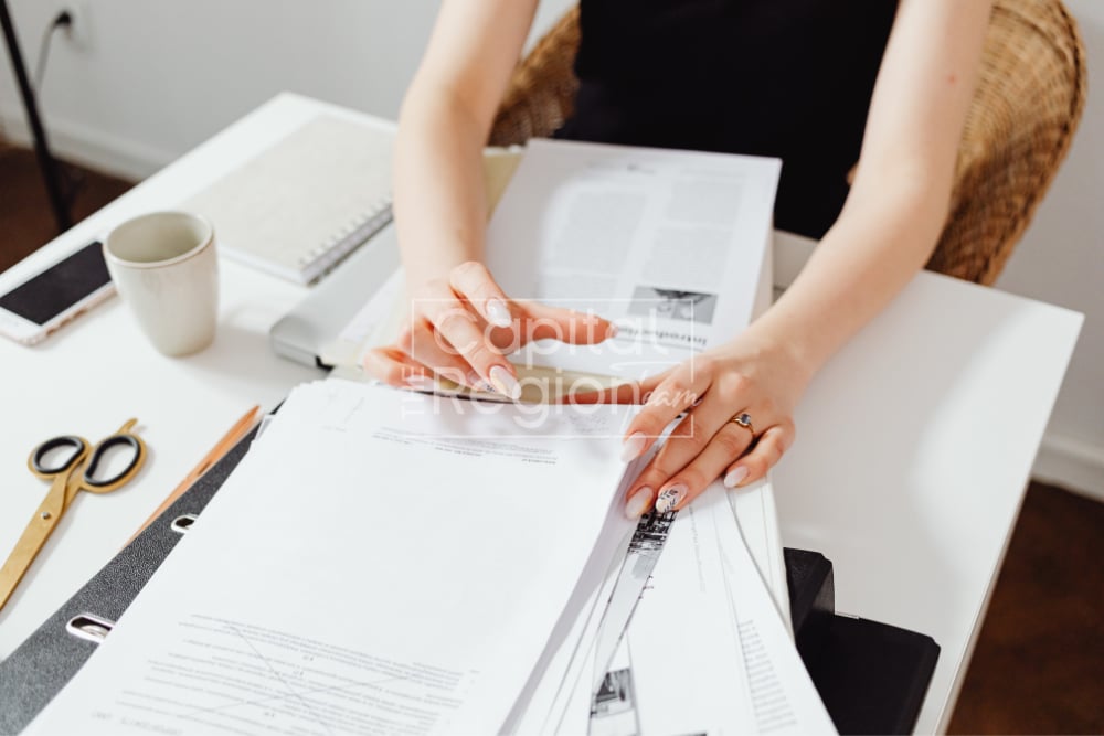 A person reviews home-buying paperwork at a desk beside a tablet and coffee cup.