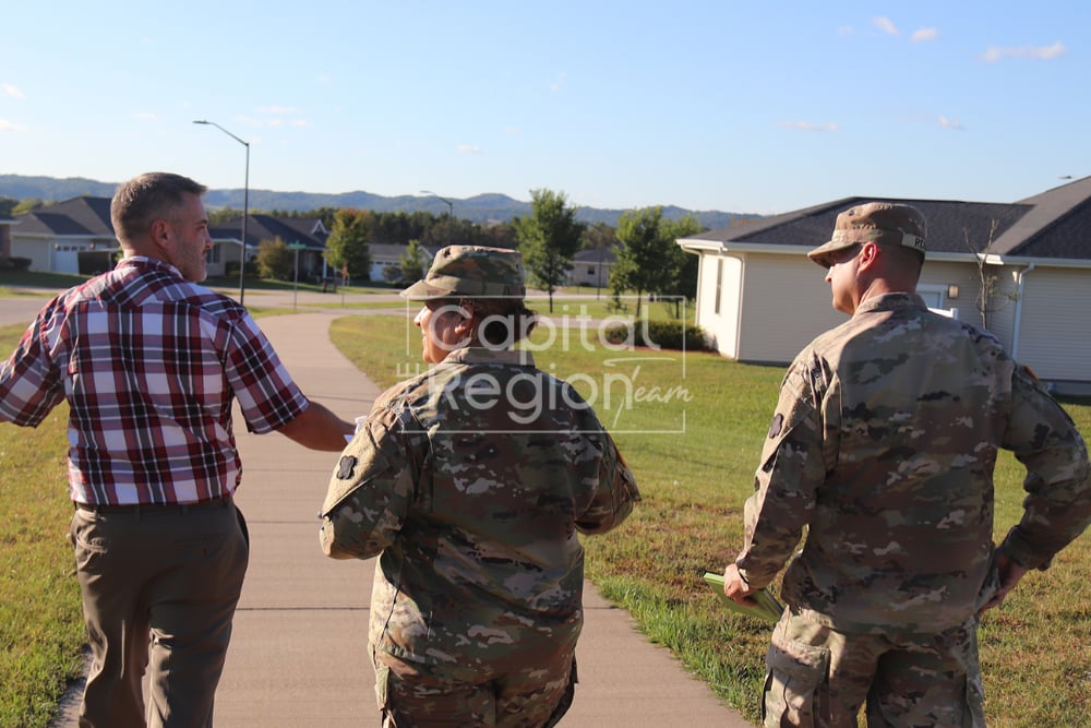 Three people walk through a residential neighborhood, including two in camouflage military uniforms.