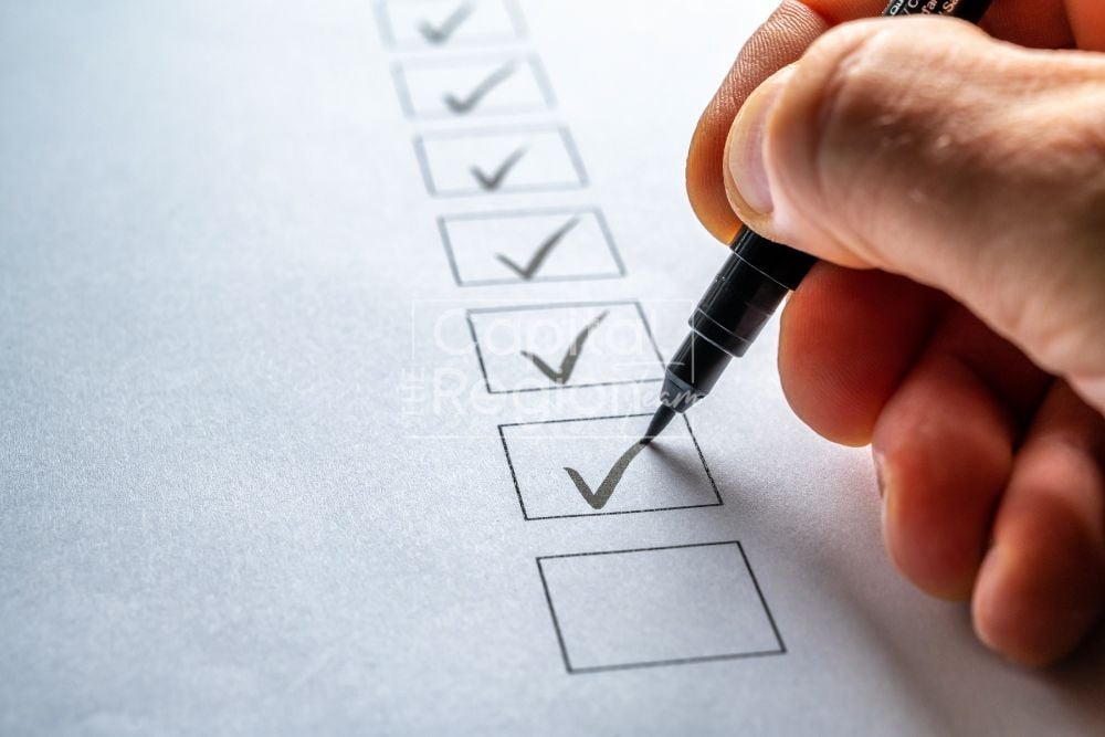 Hand marking a checked box on a paper checklist with a black pen.