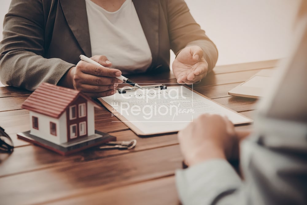 People review home-buying paperwork beside a model house.