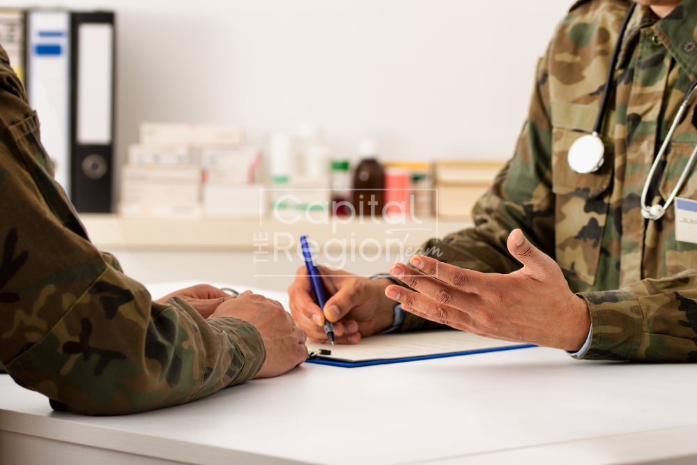 Two people in camouflage uniforms review paperwork; one wears a stethoscope.