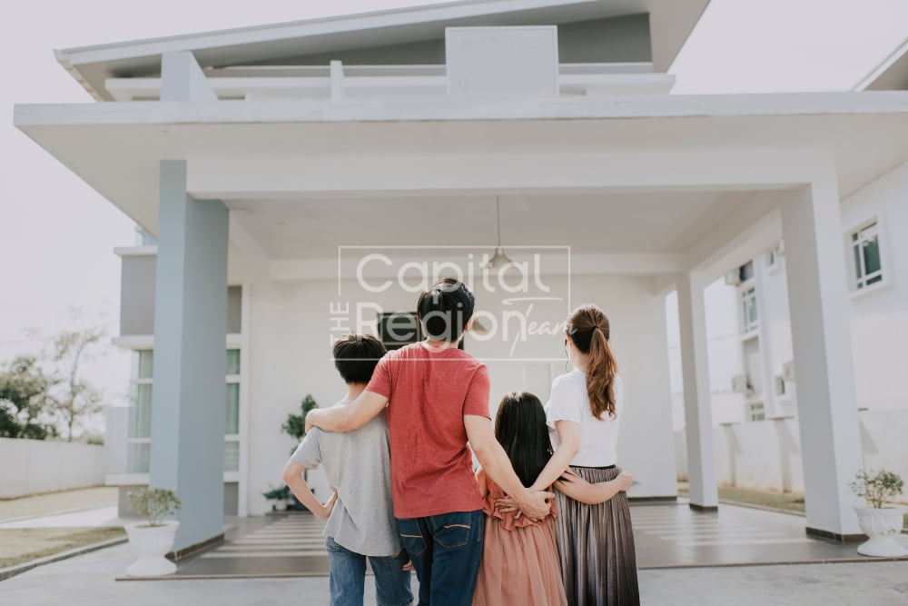 A family of four looks toward a modern white home beneath its broad covered entrance.