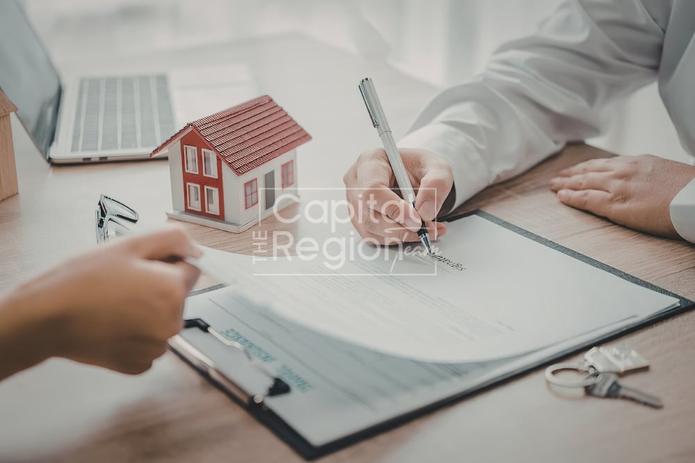 People sign home purchase paperwork beside a model house and keys.