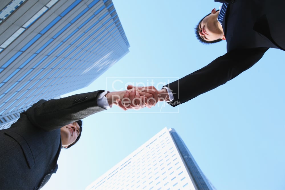 Two businesspeople shake hands beneath modern office towers.