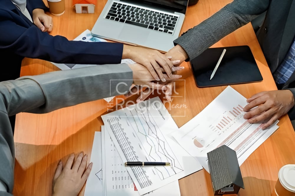 People stack hands over charts and papers on a wooden table.