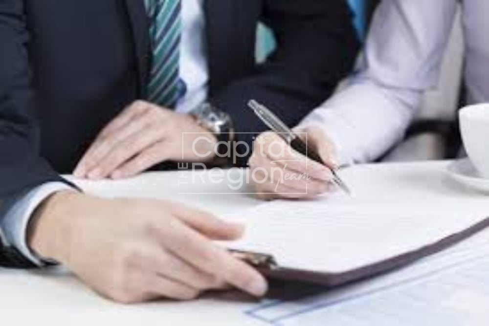 Two people signing paperwork at a table, with one holding the document.