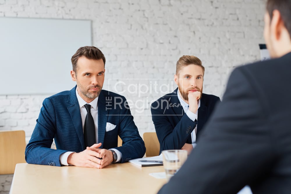 Two suited men listen during a business meeting across a table.
