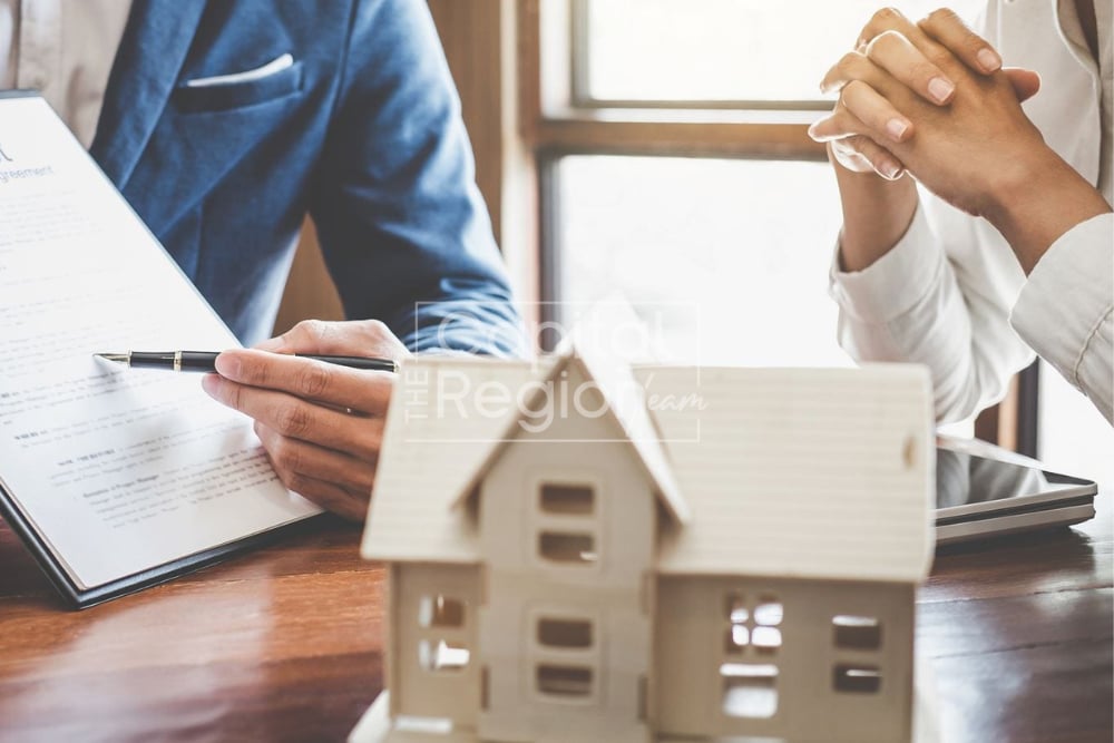 People review and sign real estate paperwork beside a model house.