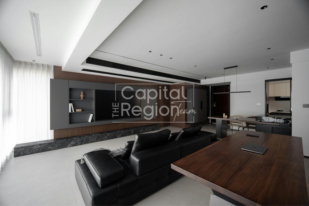 Modern living room with a black leather sectional, wood coffee table, and open kitchen.