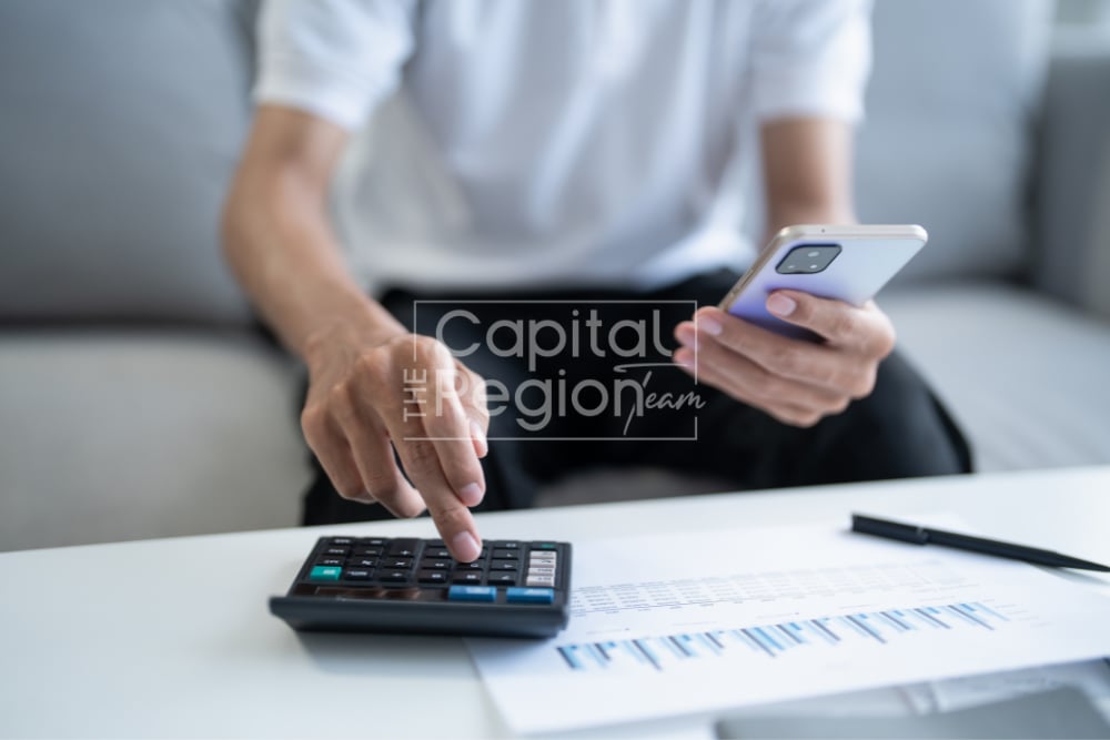 A person uses a calculator on financial charts while holding a smartphone.