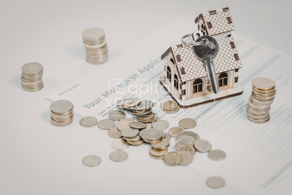 Miniature house and key on mortgage paperwork, surrounded by stacks and scattered coins.