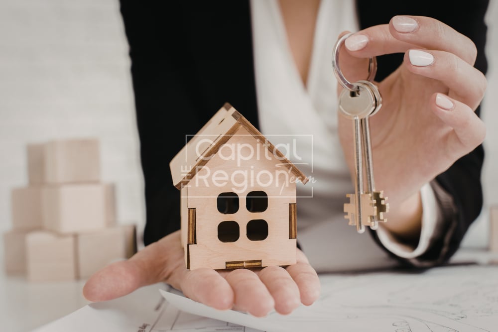 Hands present a small wooden house model and a key.