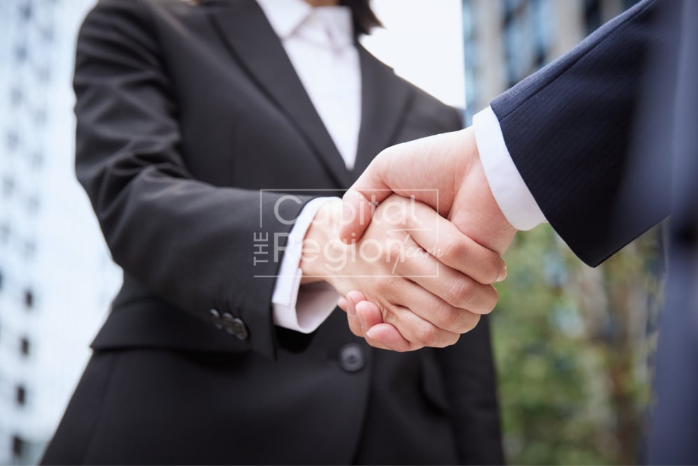 Two people in business suits shake hands during a negotiation.