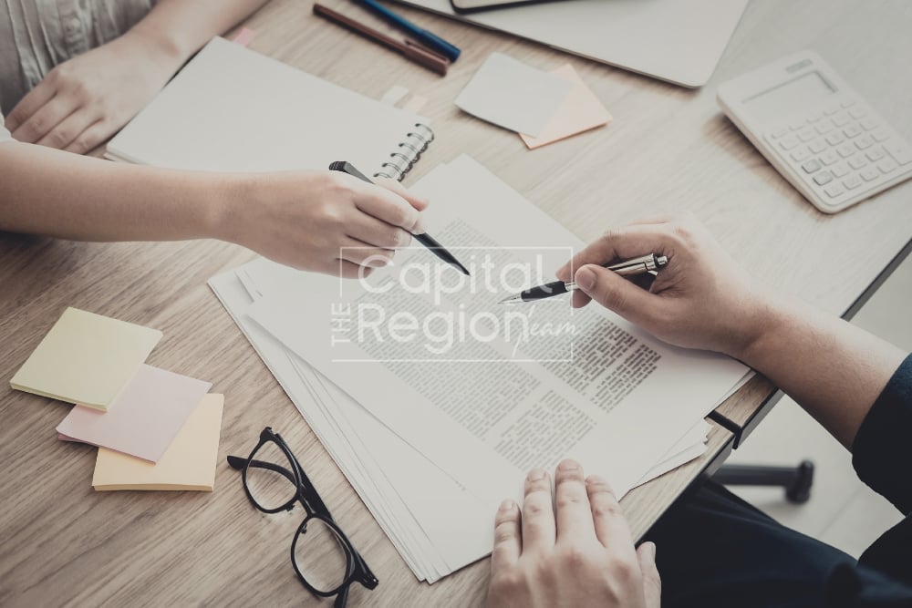 People review and sign paperwork together at a desk, with pens, a calculator, and notes nearby.