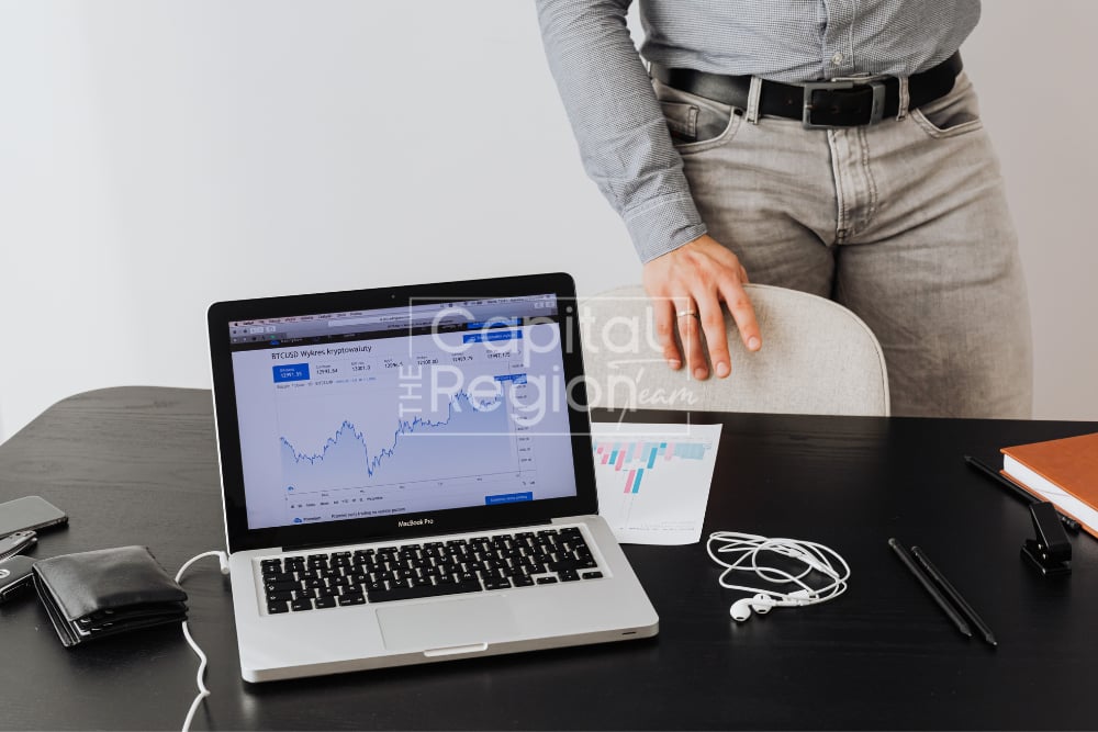 Person standing beside a desk with a laptop displaying a financial chart.