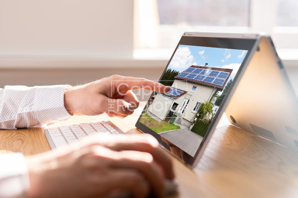 A person uses a tablet to view a solar-panel home while working at a desk.