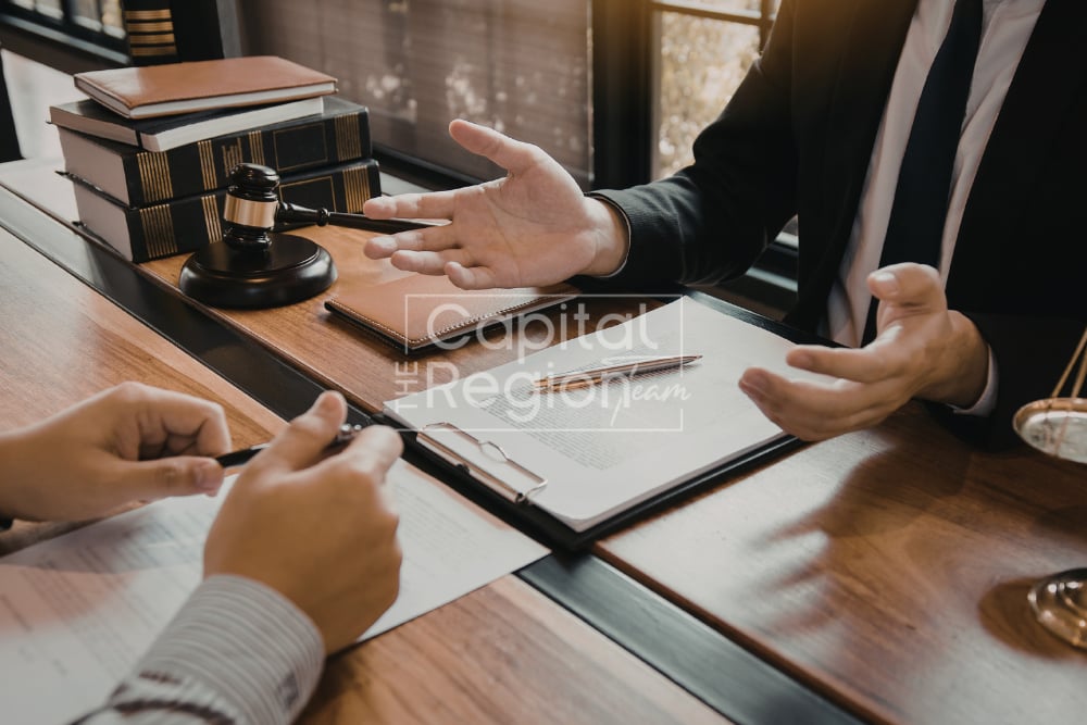 People review contract paperwork across a desk beside a gavel and stacked books.