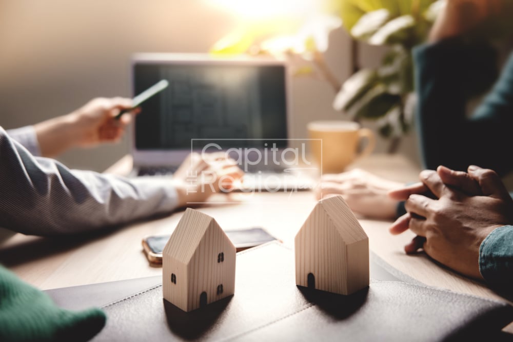 People negotiate a home purchase around a table with two wooden house models.