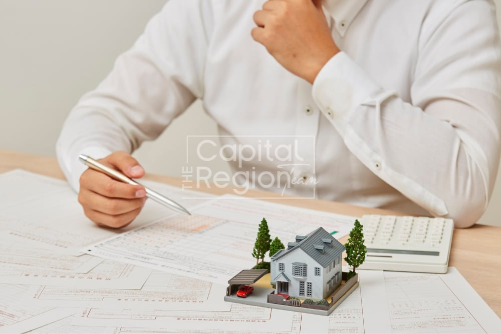 Person reviewing real estate paperwork beside a miniature house and calculator.