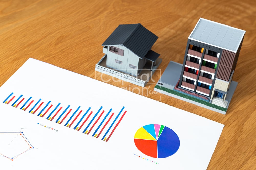 Miniature house and apartment models beside colorful market charts on a wooden table.