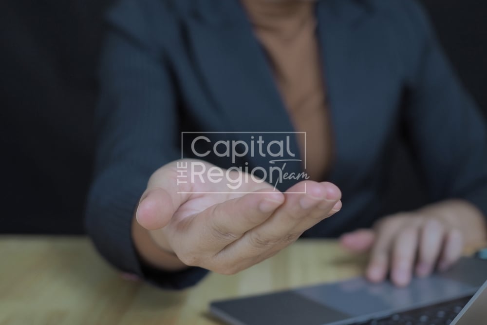 A businessperson extends an open hand over a desk beside a laptop.