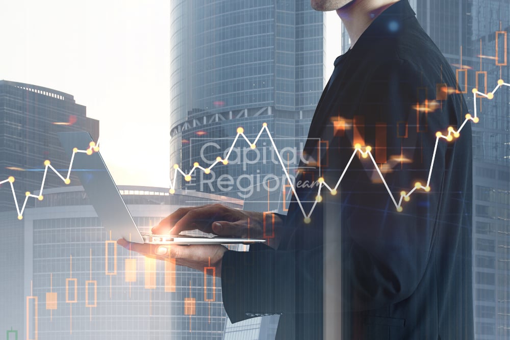 Businessperson using a laptop with financial charts overlaid against glass skyscrapers.