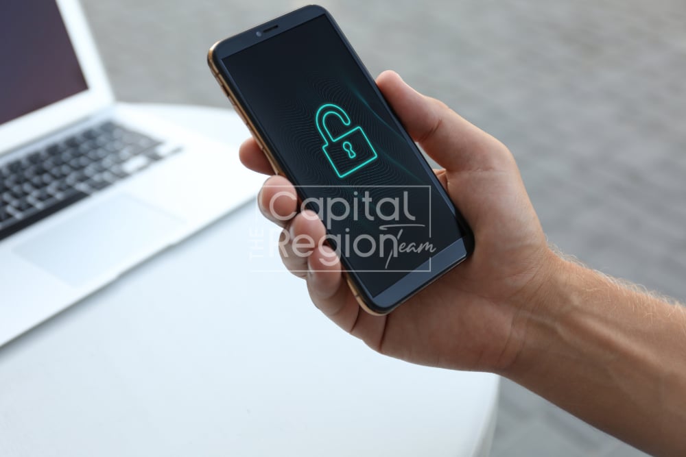Hand holding a smartphone with a glowing open padlock beside a laptop.