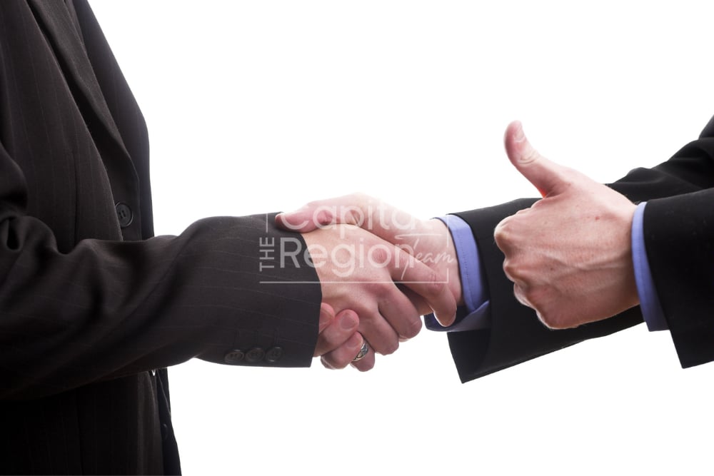 Businesspeople shake hands as one gives a thumbs-up.