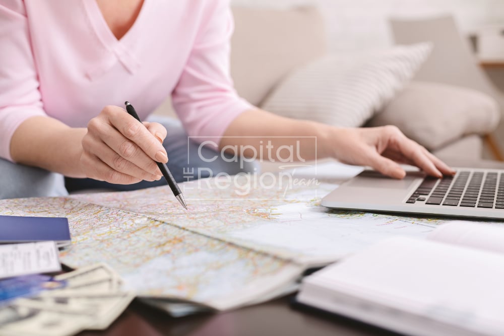 Woman marks a map with a pen beside a laptop and relocation papers.