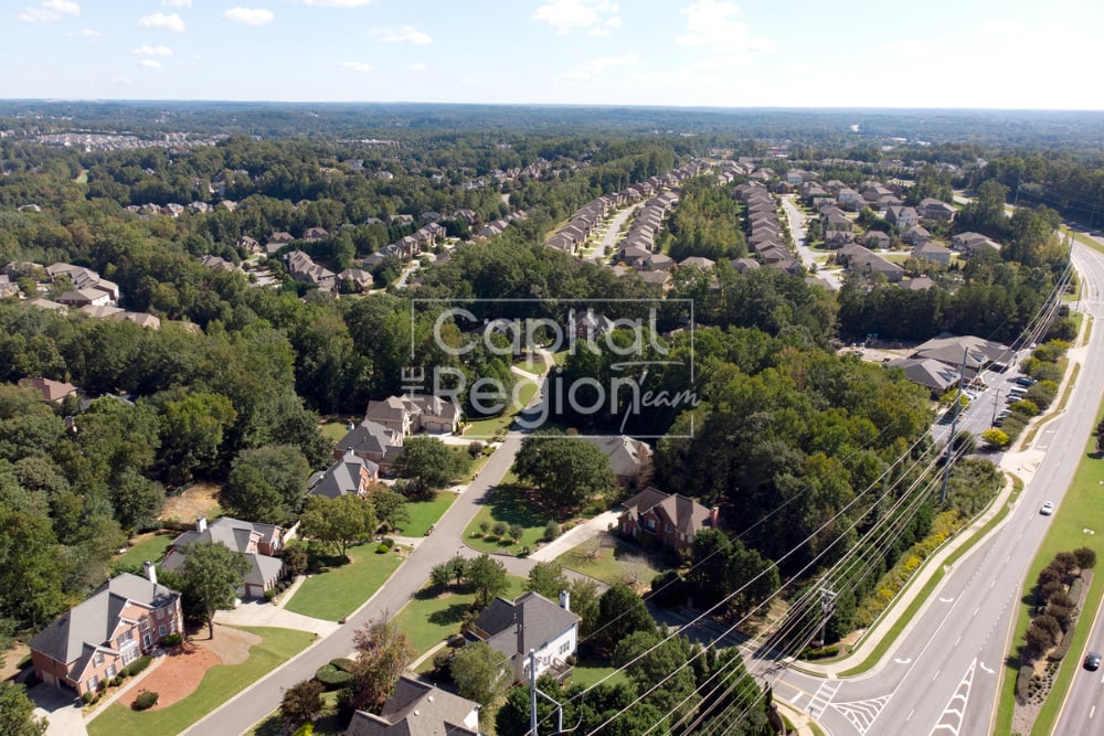 Aerial view of a tree-lined neighborhood with detached homes beside a wide road.