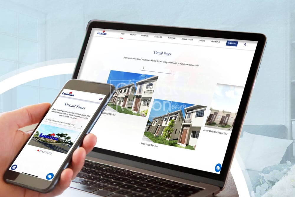 A hand holds a phone beside a laptop displaying virtual tours of modern homes.