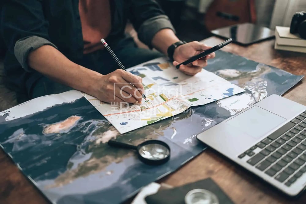 People studying maps with a pencil, smartphone, laptop, and magnifying glass.