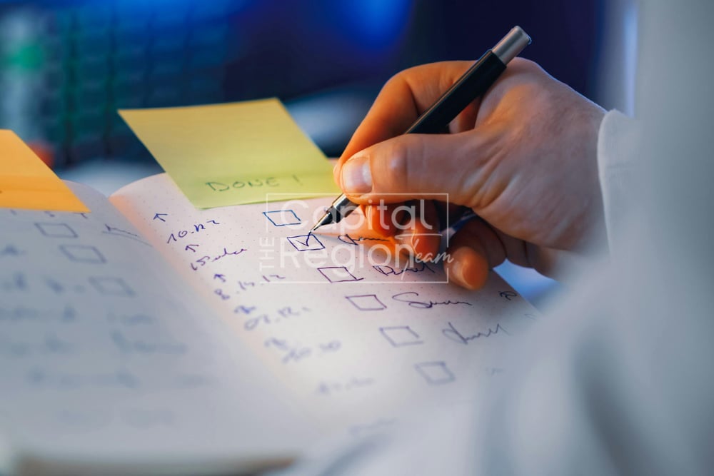 A hand marks a handwritten checklist with a pen beside colorful sticky notes.