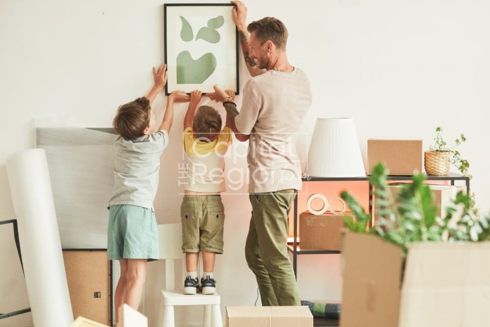 A father and two children hang framed artwork amid moving boxes.